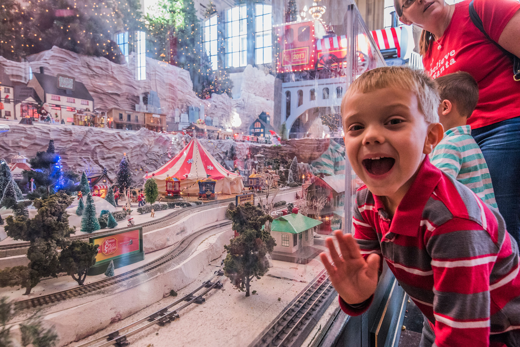 Photo of boy waving in front of model train display